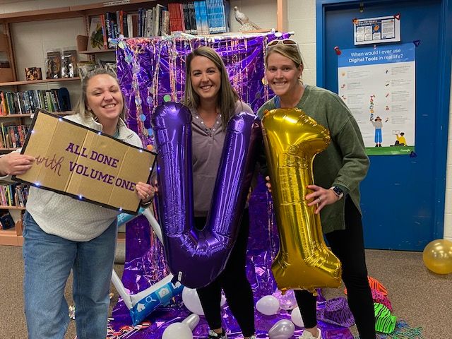 Three people holding up a sign that says all done with volume one and balloons